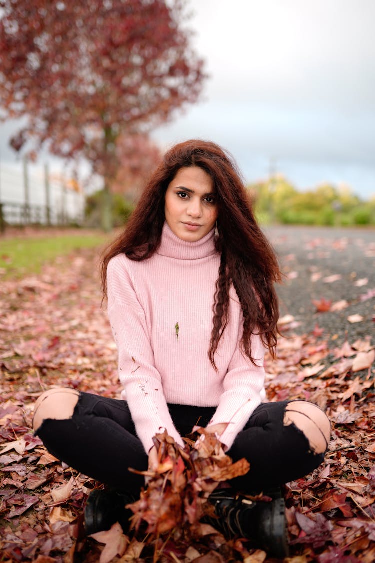 Woman In A Sweater Sitting On A Street Playing With Leaves