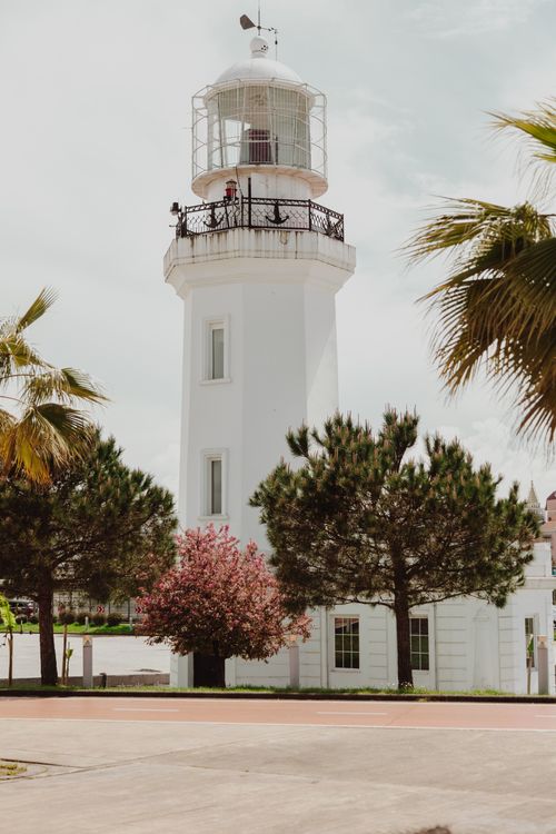 Free A picturesque lighthouse with palm trees and clear skies, perfect for travel and architecture themes. Stock Photo