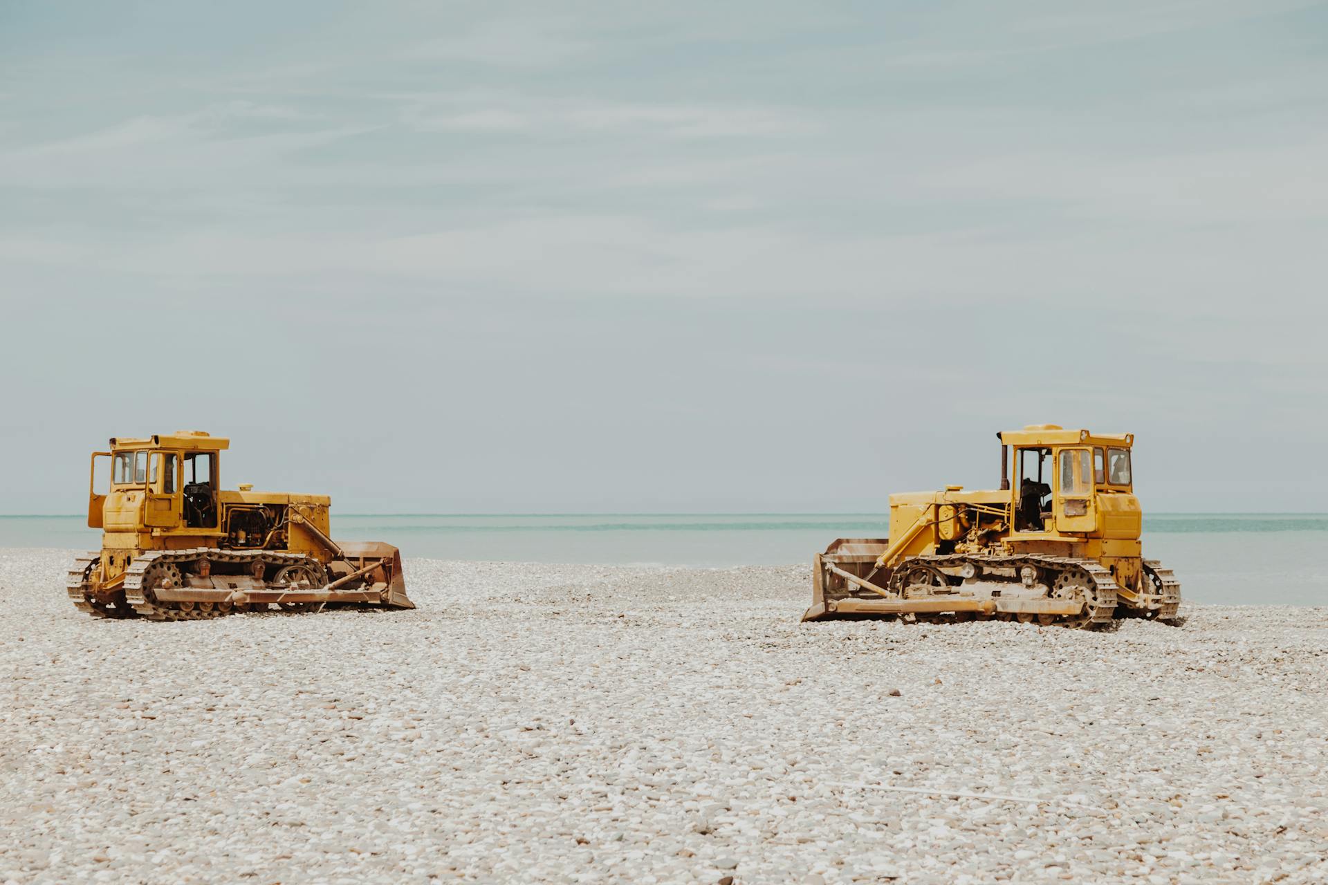 Two yellow bulldozers on a pebble beach by the sea on a calm day.