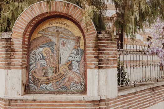 A detailed mosaic art set in a brick arch outdoors, depicting a religious scene with vibrant colors.