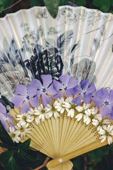 Beautiful handheld fan adorned with purple and white flowers in a traditional design.