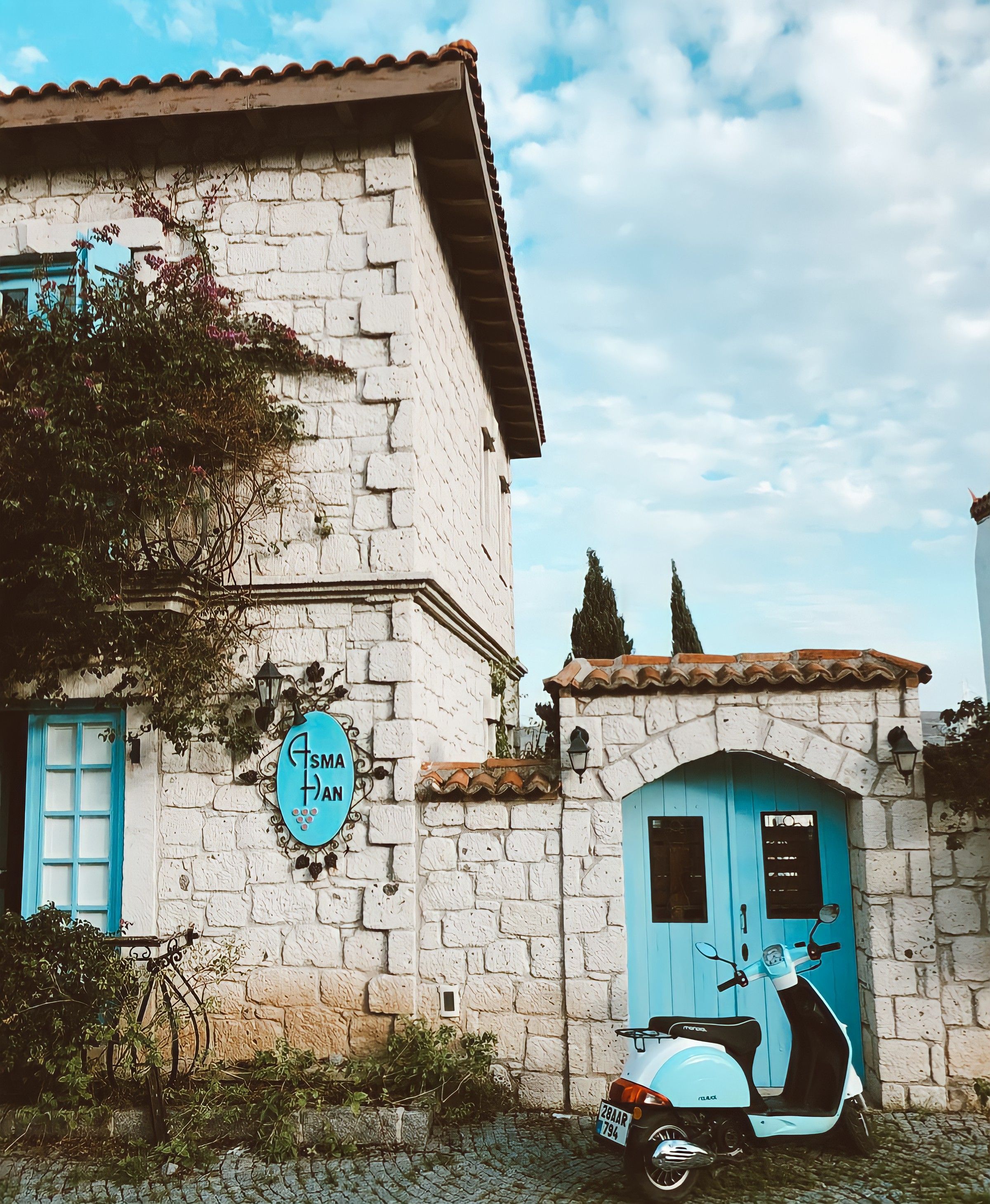 Stone house with blue doors and motor scooter parked outside, under a clear sky.