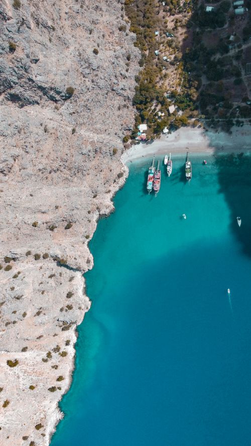 Free Explore the stunning aerial view of turquoise waters and anchored boats by rocky cliffs, perfect for summer vibes. Stock Photo