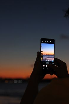 Hand holding a smartphone capturing İstanbul sunset with scenic view in background.