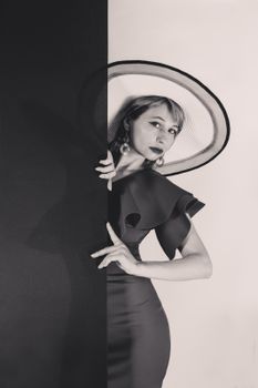 Elegant black and white portrait of a stylish woman in a large hat posing indoors.