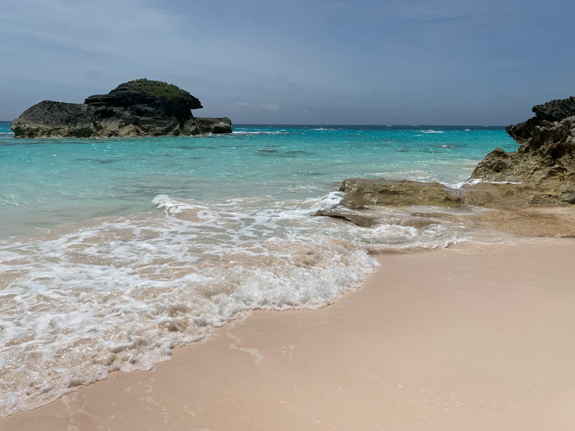 A serene sandy beach in Bermuda featuring turquoise waters and unique rock formations.