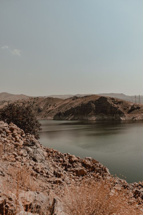 Free Tranquil lake surrounded by rocky landscape under a clear gray sky in the countryside. Stock Photo