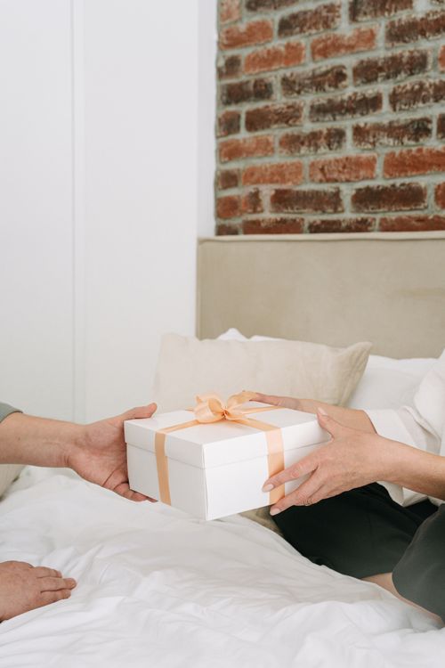 Free Two people exchanging a wrapped gift box on a bed, symbolizing celebration and care. Stock Photo