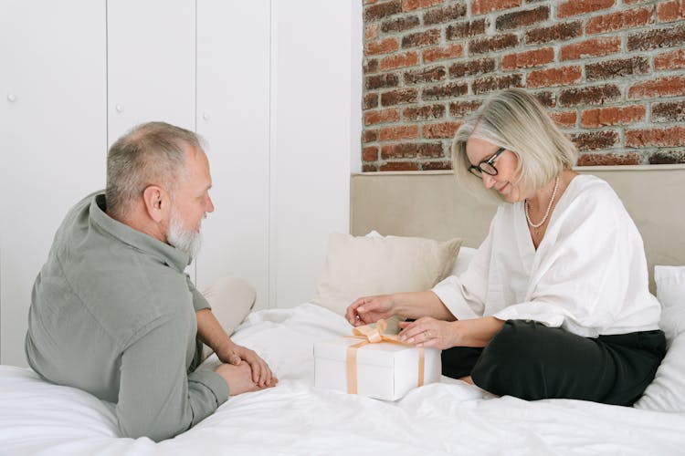 Elderly Woman Sitting On Bed Looking At A Gift