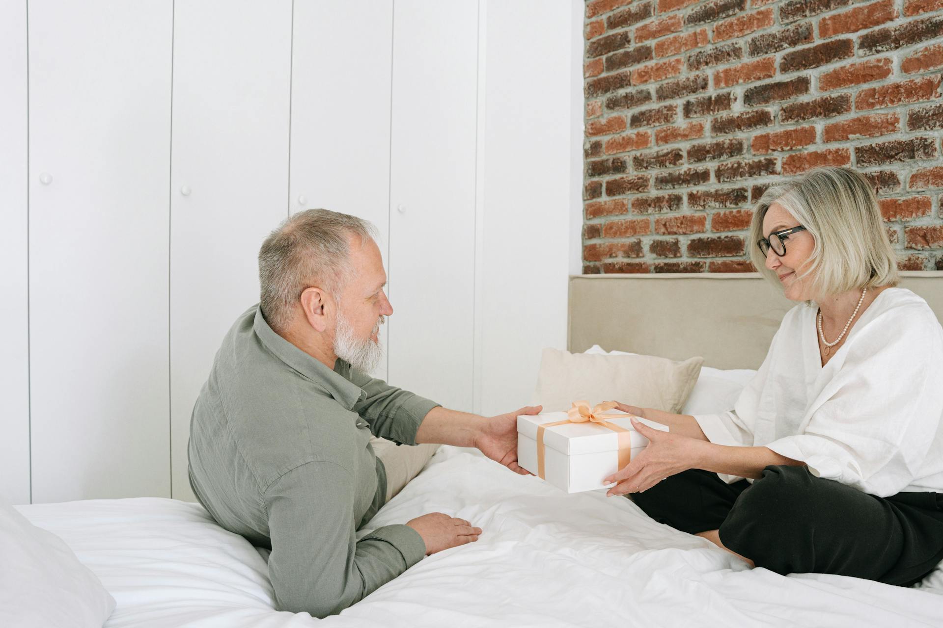 A senior couple sharing a gift on a cozy bed in a bright, modern bedroom setting.