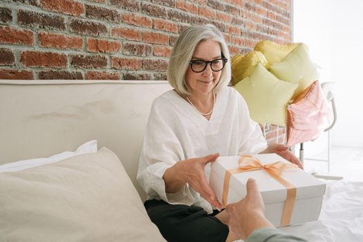 Elderly woman happily receives a gift with balloons in a cozy room setting.