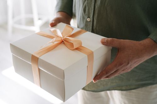 Free A person holding a white gift box tied with a peach ribbon, symbolizing celebration and surprise. Stock Photo