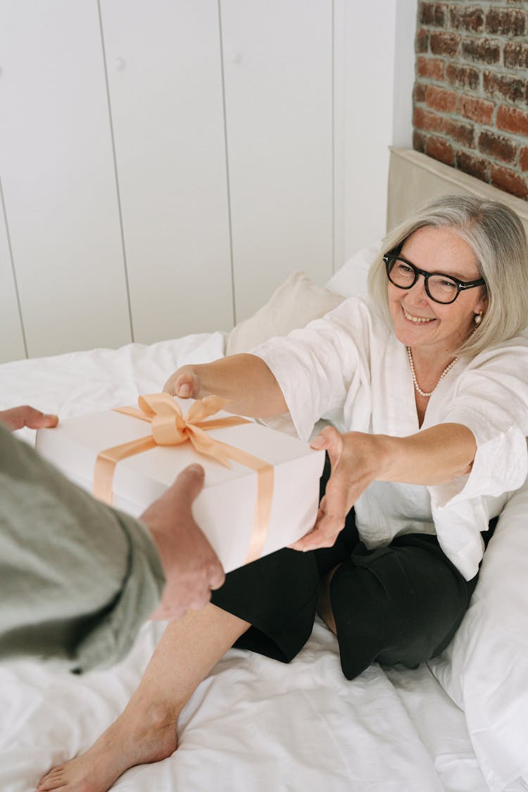 Person Giving Gift To An Elderly Woman Sitting On Bed