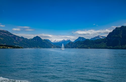 Free White Sailboat on Sea Near Mountain Under Blue Sky Stock Photo