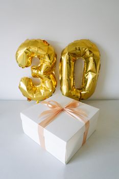 A stylish 30th birthday celebration scene with gold balloons and a wrapped gift box.