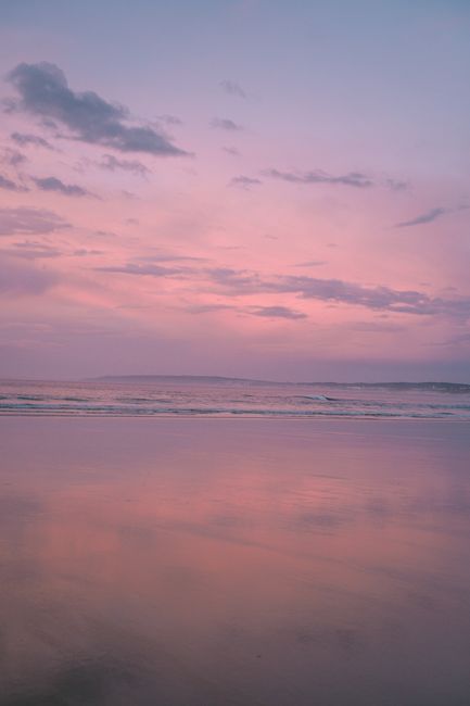 Tranquil beach scene in Portugal at sunset with pastel sky and calm waves.