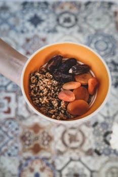 Top view of a hand holding a bowl with dried fruits and granola.