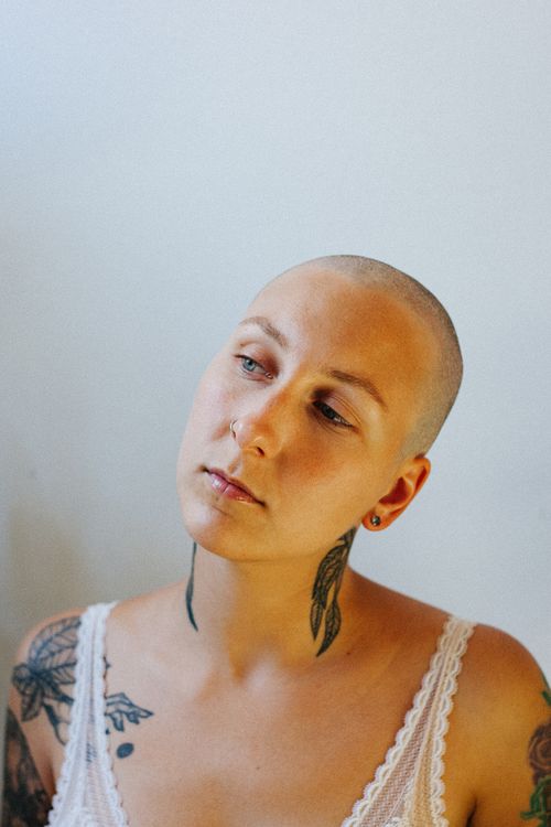 Free A thoughtful woman with tattoos and shaved head against a minimalist background. Stock Photo