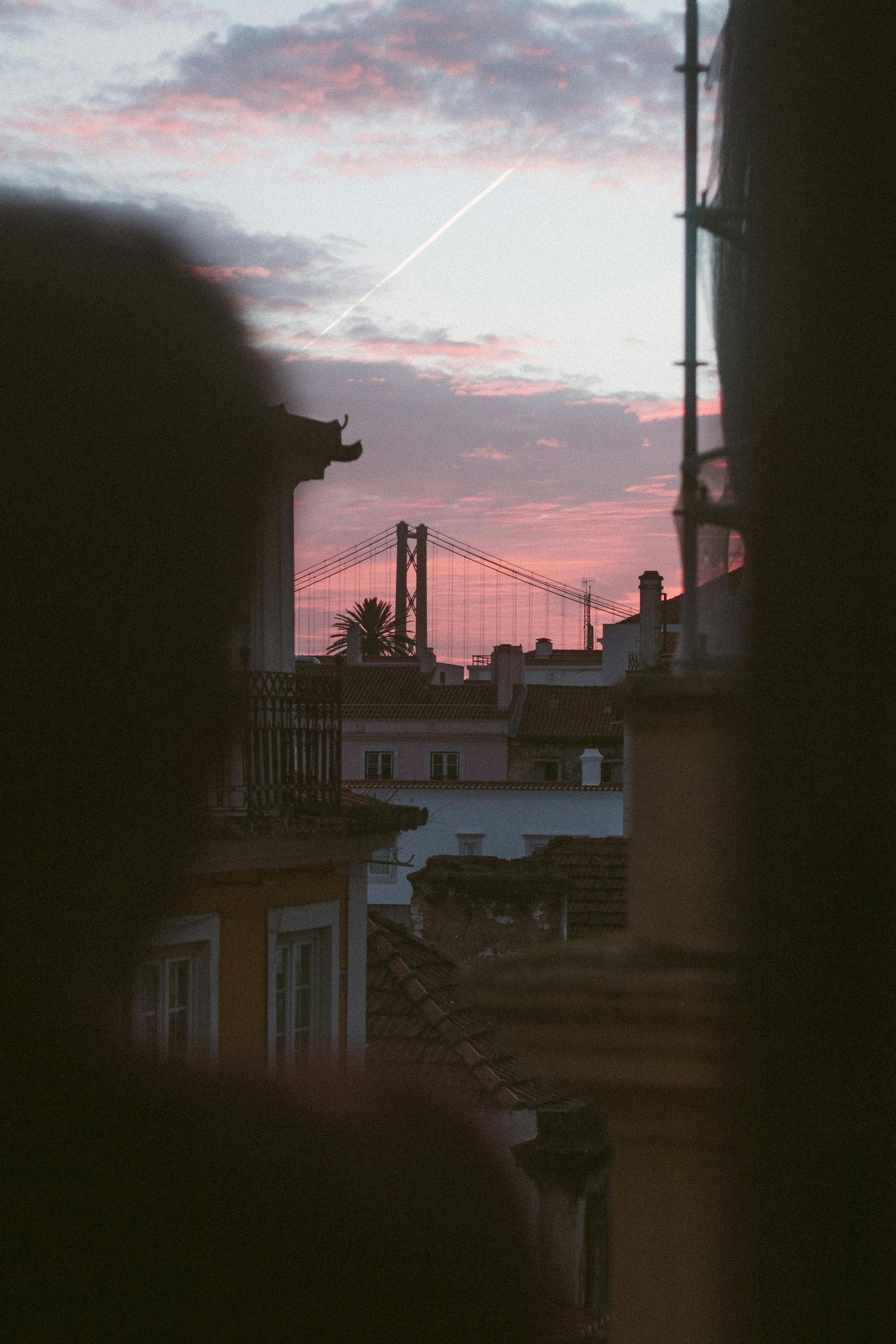 Free Silhouette of a man looking at Lisbon's 25 de Abril Bridge at sunset, framed by a window. Stock Photo