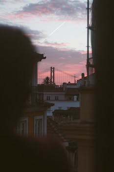 Silhouette of a man looking at Lisbon's 25 de Abril Bridge at sunset, framed by a window.