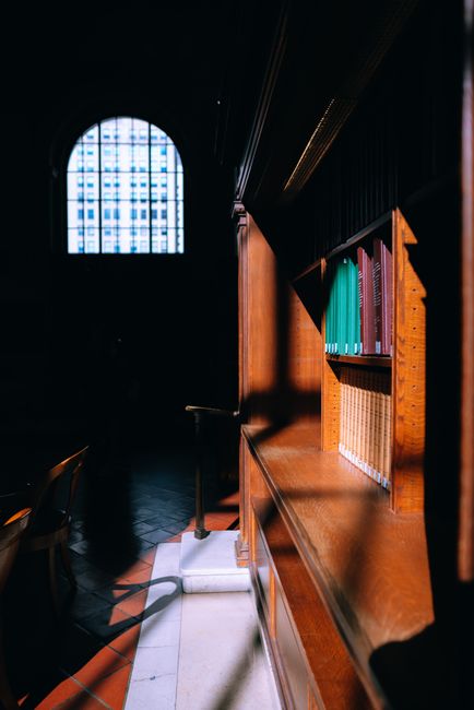Sunlight casts shadows on a wooden bookshelf in a quiet library setting.