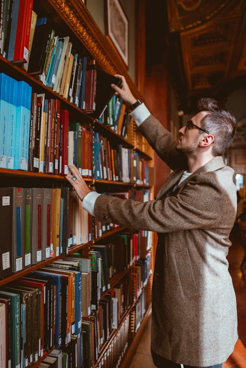 Man in Brown Coat Standing in Front of a Bookcase