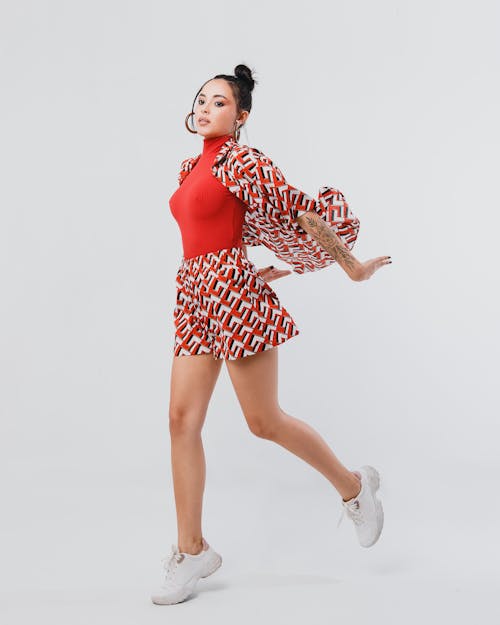 Full body of active female with black hair in trendy outfit and sneakers jumping on white background in light studio