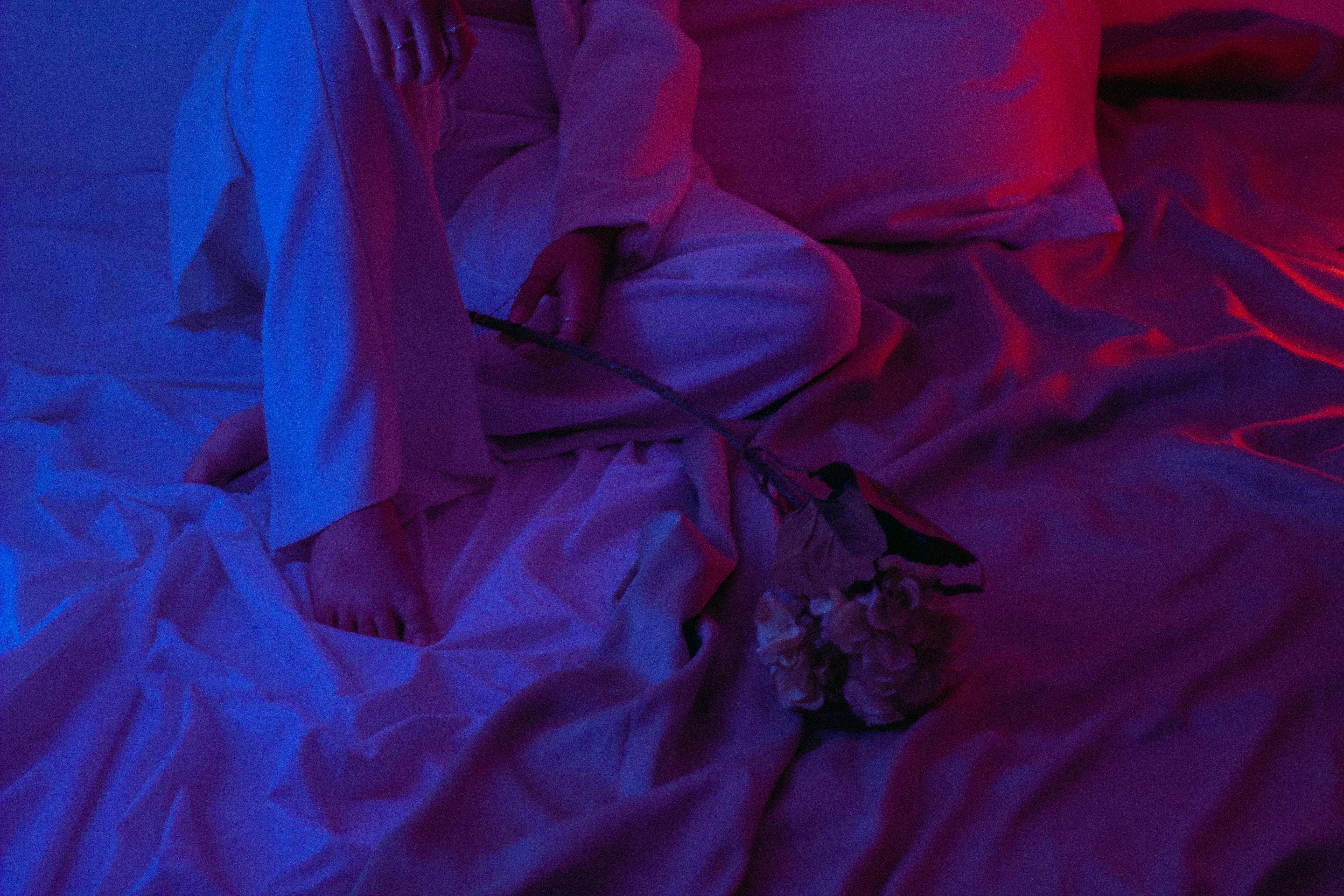 A creative portrait with dramatic red and blue lighting on draped fabric and a delicate flower.