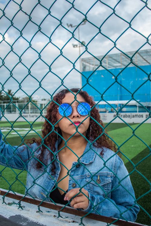 Free Woman wearing sunglasses looks through a chain link fence on a sports field. Stock Photo