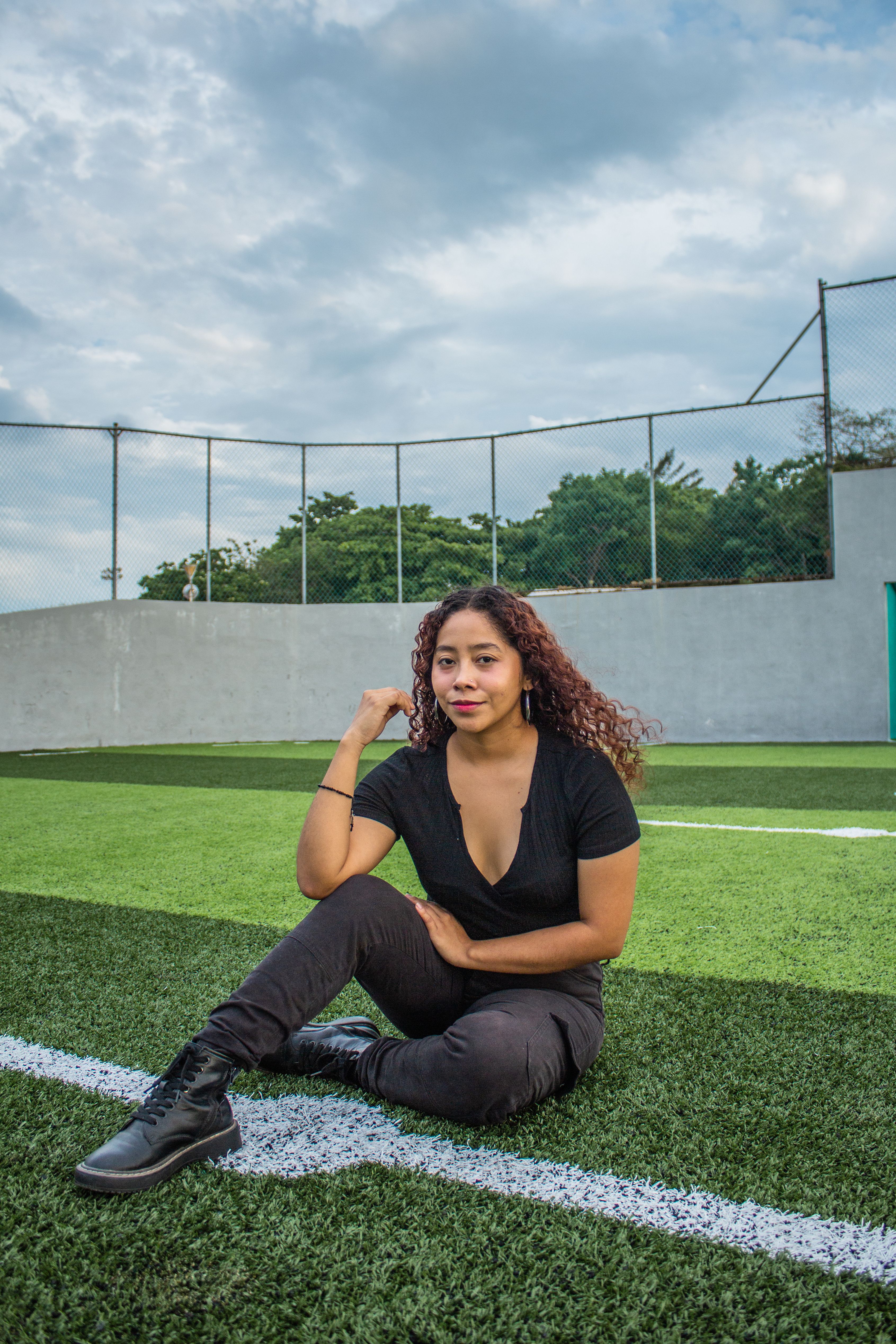Woman posing confidently on a green sports field on a sunny day.