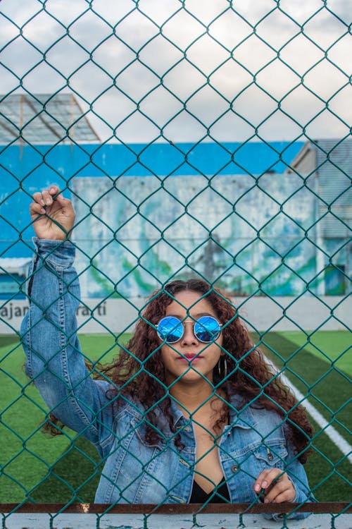 Free Woman in Blue Denim Jacket Holding on a Fence Stock Photo