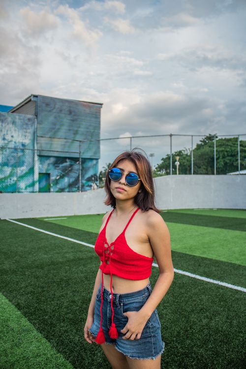 Free Stylish young woman in red top and denim shorts posing on a sports field Stock Photo