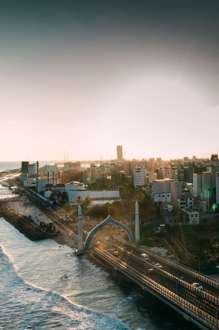 Modern suspension bridge with cars located near foamy waving sea and city with residential buildings against cloudless in coastal area
