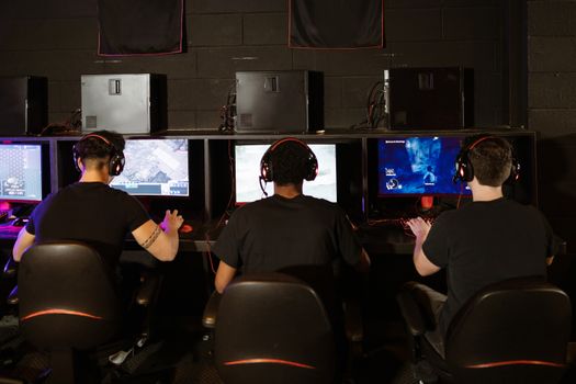 Three men focused on an intense PC gaming session in a modern esports arcade, enjoying teamwork and strategy.