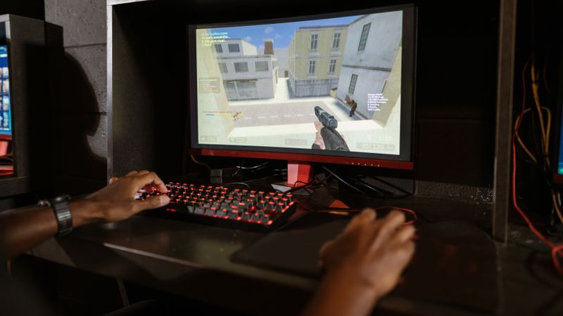 Person engaging in a shooting video game on a high-performance setup with mechanical keyboard.