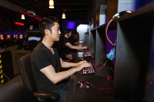 Focused young man playing video games on a mechanical keyboard in a cyber gaming setup.