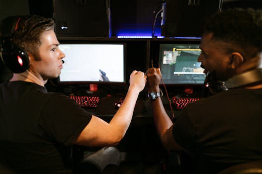 Two male friends fist bump at a computer gaming station, showcasing teamwork and camaraderie.