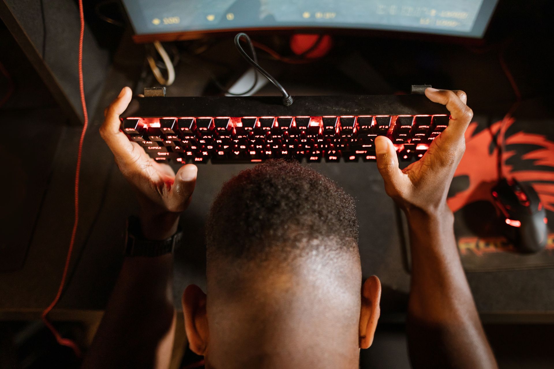 Gamer expresses frustration with video game by holding up keyboard. Overhead shot of gaming setup.