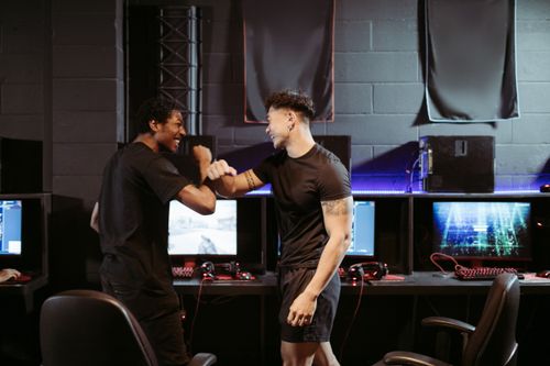 Free Two friends celebrating a win in a gaming arcade, showcasing excitement and joy. Stock Photo