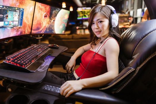 A woman engaged in gaming at a high-tech setup with dual monitors and white headphones.
