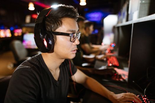 Young man with headphones gaming in a lively internet cafe, deep in concentration.