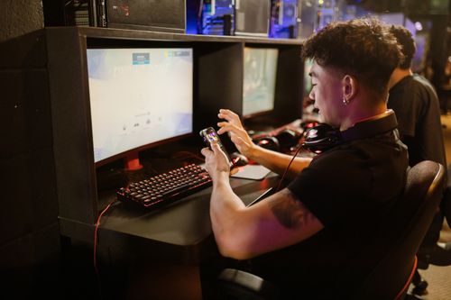Free A young man is gaming using a smartphone and a PC setup with a mechanical keyboard indoors. Stock Photo