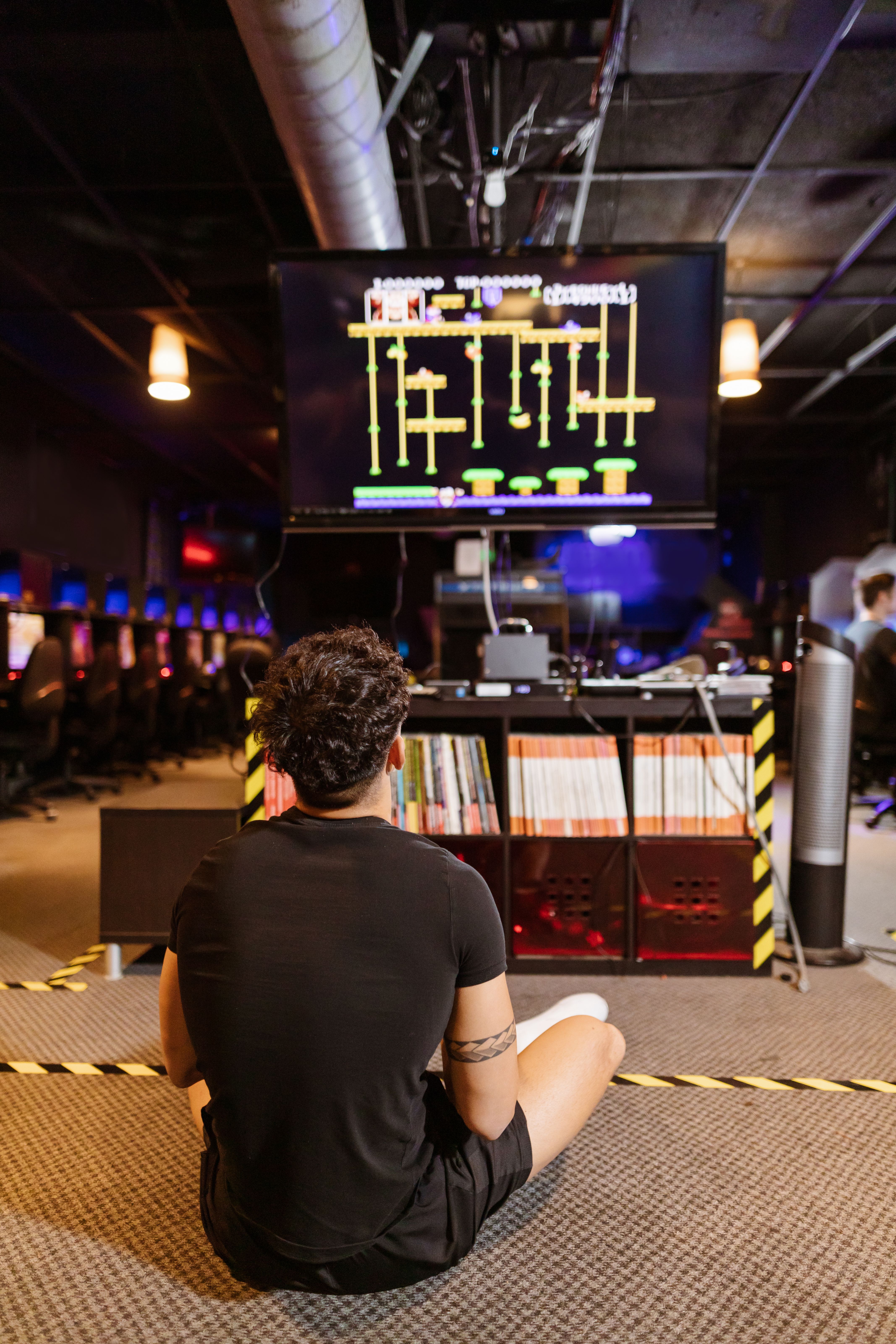 A young man sitting in an arcade, playing a classic retro video game on a large screen.