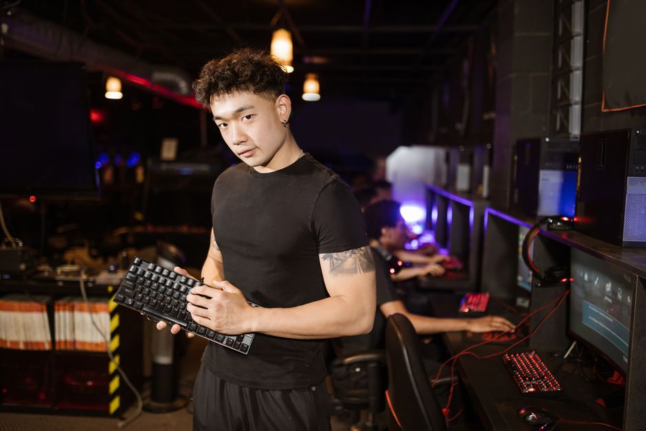 A young man in a black shirt holding a keyboard in a modern gaming cafe, showcasing e-sports culture.