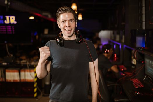 Smiling man with headphones and fist raised, celebrating in a gaming arena.