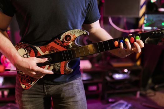 Close-up of a man playing a Guitar Hero controller indoors, featuring vibrant colors and technology.