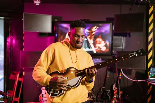 A man in a yellow hoodie plays a guitar simulation game indoors, immersed in gaming fun.