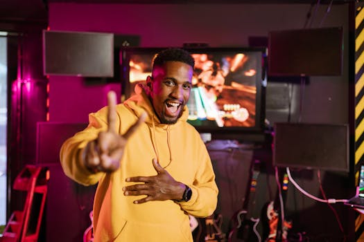 Black man in yellow hoodie smiling and standing in an esports gaming room.