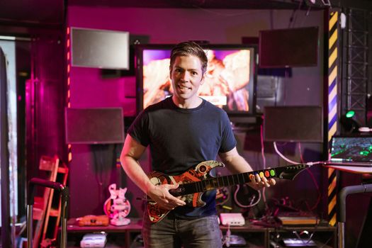 Adult male playing guitar controller in a vibrant gaming setup indoors, showcasing esports and recreation.