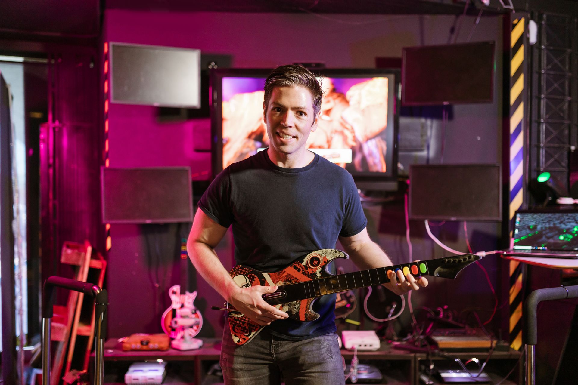 Adult male playing guitar controller in a vibrant gaming setup indoors, showcasing esports and recreation.